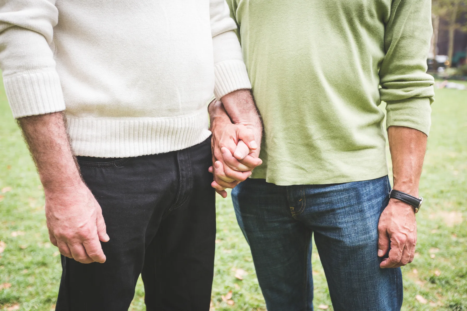Two men standing close together outdoors, holding hands as they rebuild connection.